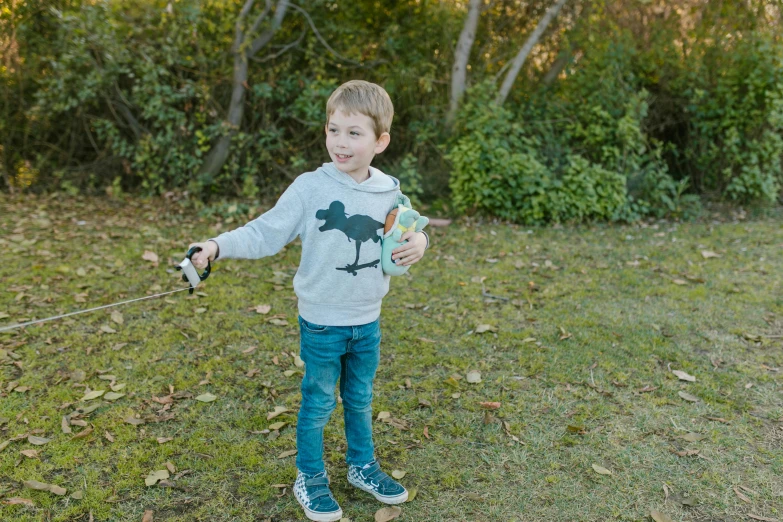 a little boy that is standing in the grass with a kite, wearing a grey hooded sweatshirt, holding a bottle, holding controller, photograph taken in 2 0 2 0