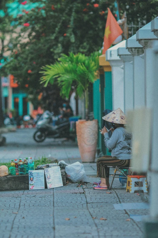 a woman sitting on a bench in the middle of a street, pexels contest winner, vietnam, outdoors tropical cityscape, square, multi colour