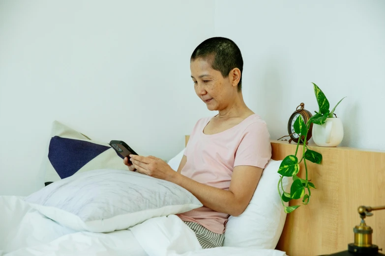 a woman sitting on a bed reading a book, inspired by Ruth Jên, happening, looking at his phone, shaved head, profile image, asian woman