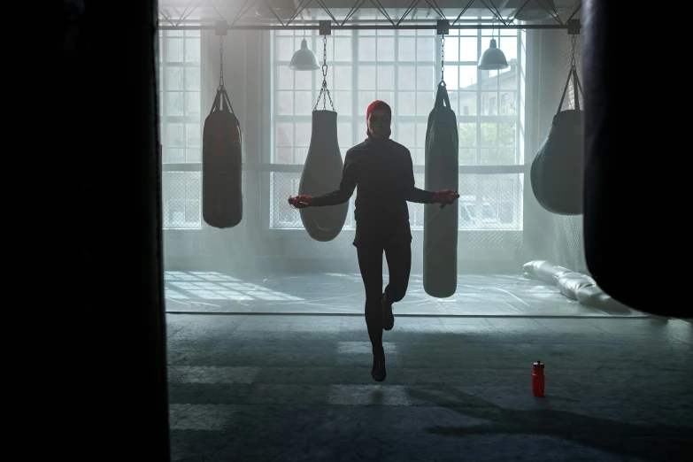 a man standing in front of a punching bag, inspired by Michael Komarck, pexels contest winner, light and space, movie still of emma watson, solo performance unreal engine, back lit, in a gym