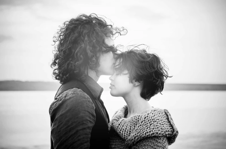 a man and a woman standing next to each other, a black and white photo, by Karl Buesgen, pexels, romanticism, curly bangs, lesbian kiss, shoreline, ffffound