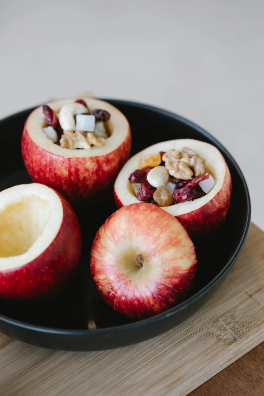 a black plate topped with apples on top of a wooden table, bowl filled with food, pod, nut, profile image