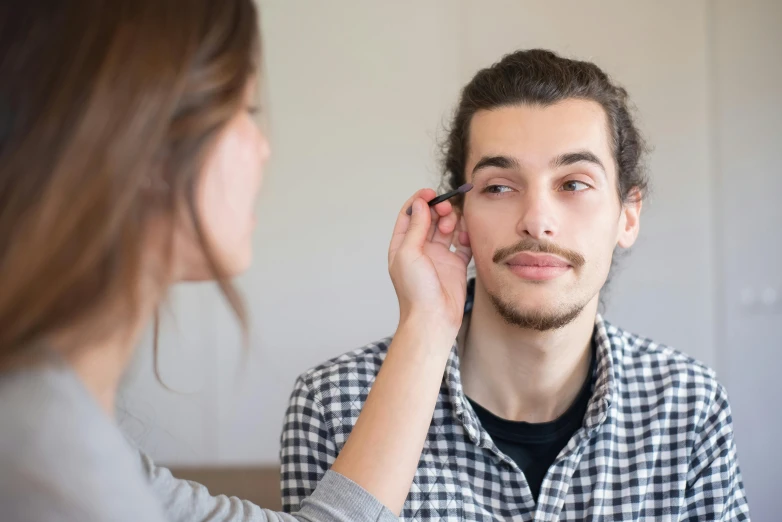 a man putting makeup on a woman's face, by Daniel Lieske, shutterstock, gauged ears, young man with short, unibrow, lachlan bailey