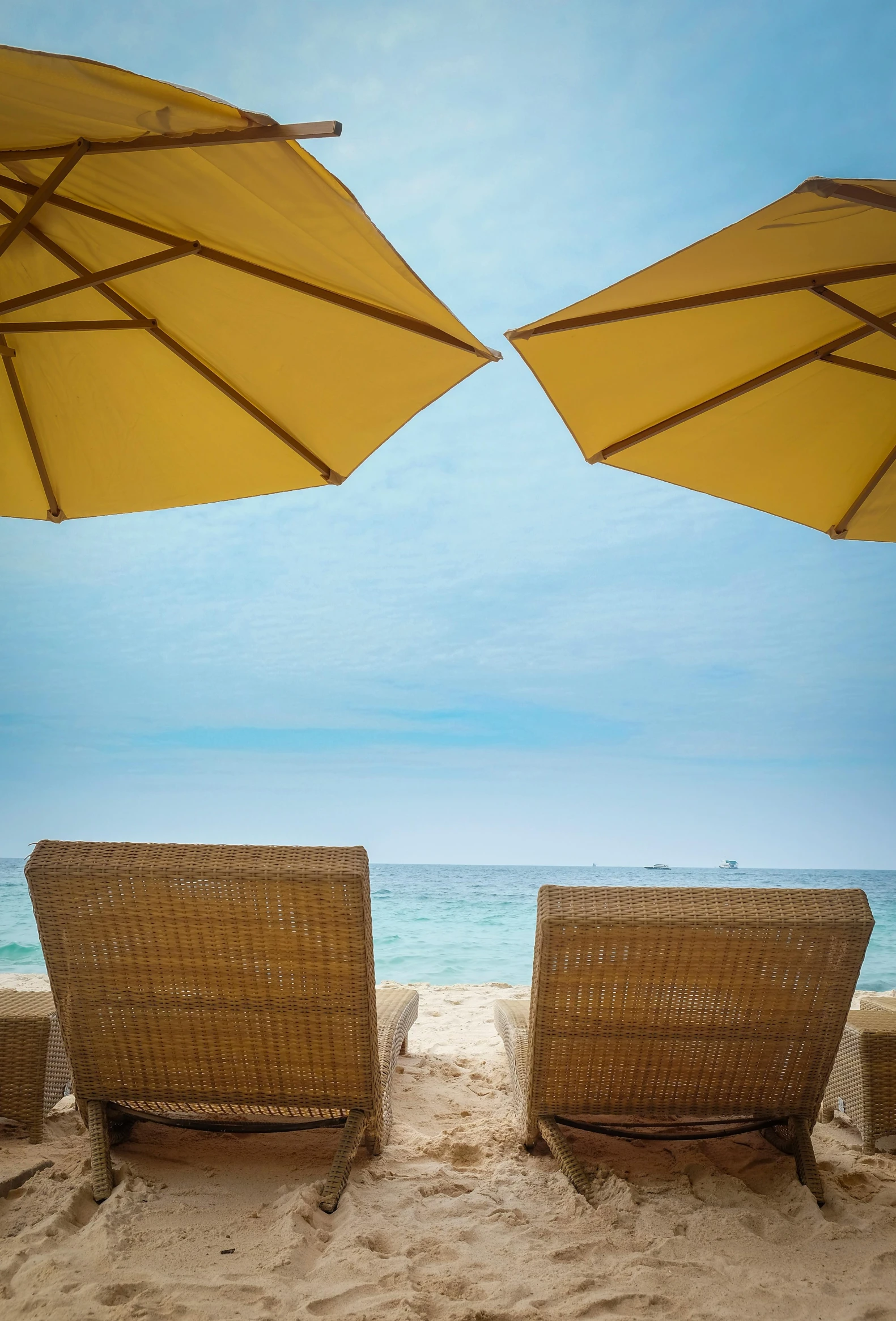 a couple of chairs sitting on top of a sandy beach, yellow parasol, some sandy yellow pillows, ocean view, lying down