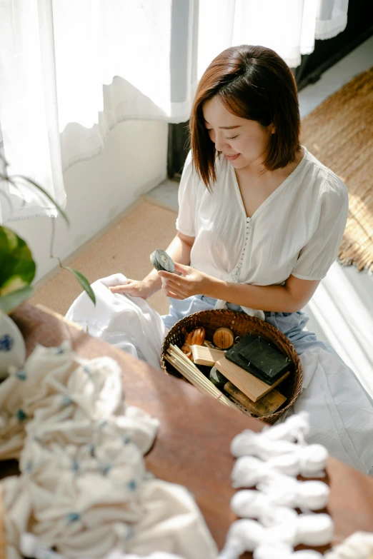 a woman sitting on the floor next to a basket of food, inspired by Cui Bai, pexels contest winner, happening, wearing a linen shirt, inspect in inventory image, natural light in room, flat lay