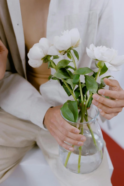 a close up of a person holding a vase with flowers, wearing white clothes, holding each other, reassuring, ignant