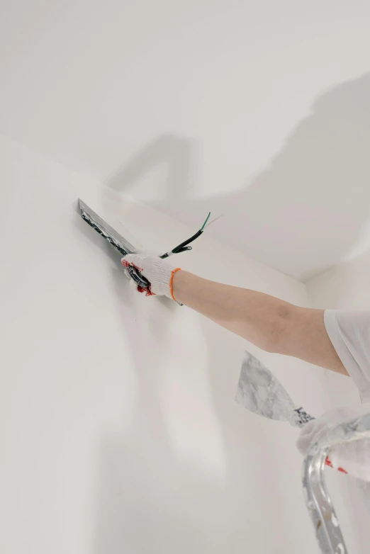 a man painting a wall with a pair of scissors, with matte white angled ceiling, paint flecks, up-close, sleek hands