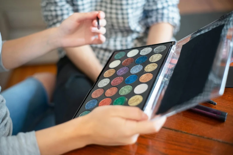 a close up of a person holding a box of makeup, a photorealistic painting, trending on pexels, metal lid, using a magical tablet, 7 0 s palette, colourised