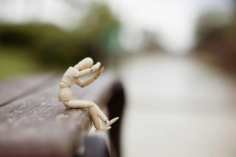 a toy sitting on top of a wooden bench, inspired by Chris LaBrooy, unsplash, street art, articulated joints, closed hands, paul barson, disappointed