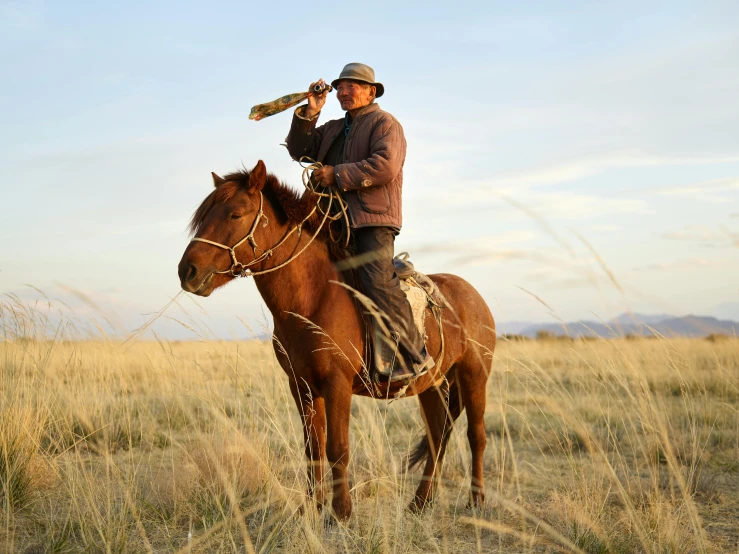 a man riding on the back of a brown horse, inspired by Frederic Remington, pexels contest winner, in the steppe, holding a wooden staff, national geographic photo shoot, having a snack