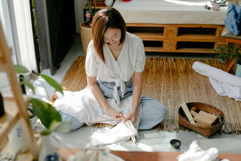 a woman sitting on the floor working on something, inspired by Kim Du-ryang, pexels contest winner, white tablecloth, avatar image, linen, yukata clothing