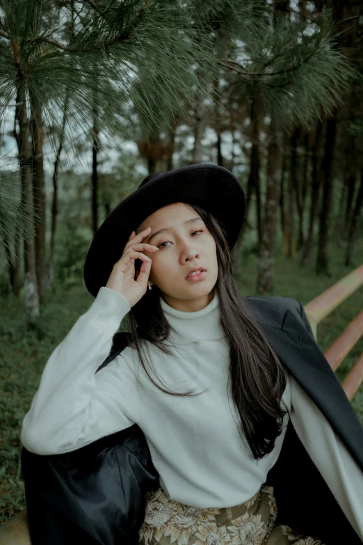 a woman in a black hat talking on a cell phone, inspired by Cheng Jiasui, trending on pexels, realism, in white turtleneck shirt, album cover, trees in the background, casual pose