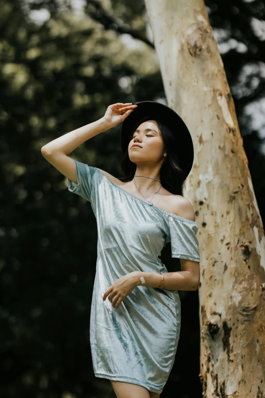 a woman standing next to a tree wearing a hat, unsplash, renaissance, wearing silver dress, singapore, casual modern clothing, metallic cyan bodysuit