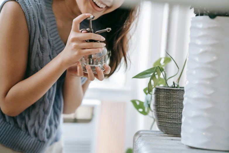 a woman holding a glass of water next to a potted plant, trending on pexels, happening, carrying a bottle of perfume, silver small glasses, joyful people in the house, grey