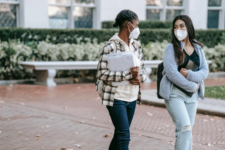 a couple of women standing next to each other on a sidewalk, trending on pexels, happening, masked doctors, school class, background image, university