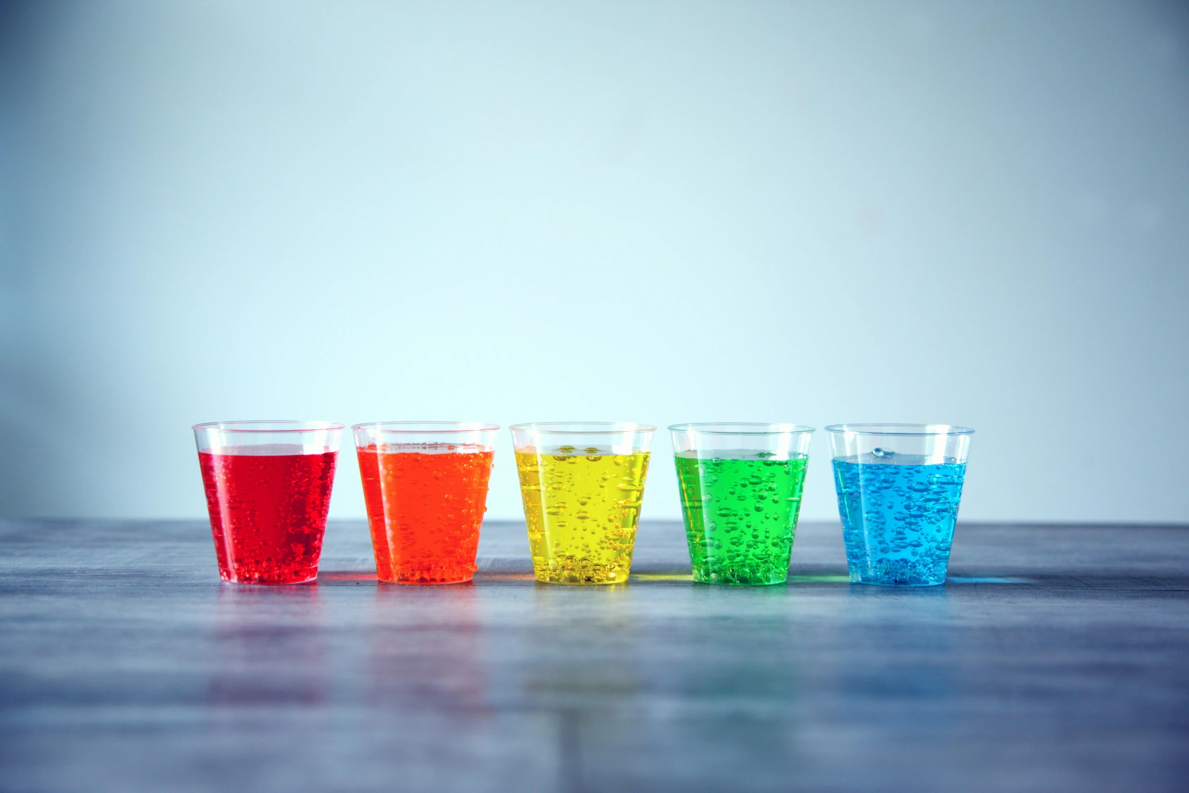 a row of glasses filled with different colored liquids, a hologram, inspired by Damien Hirst, pexels, jello, on grey background, made of drink, 5 years old