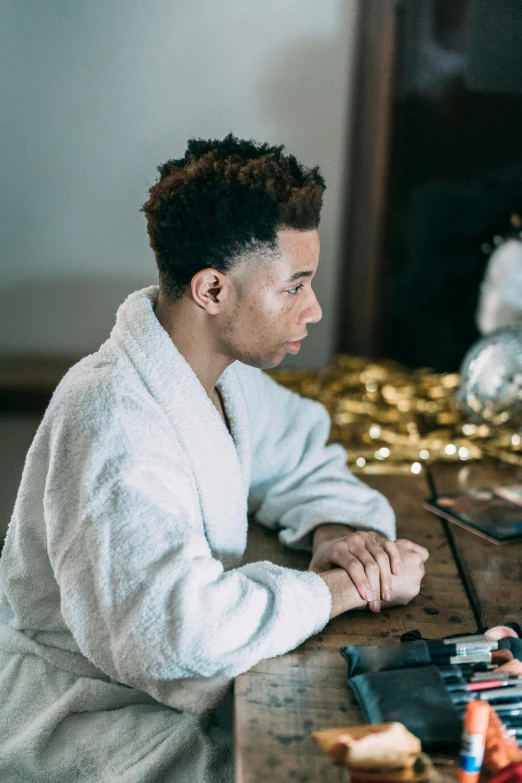 a man sitting at a table in front of a mirror, trending on pexels, white and gold robes, afro hair, male teenager, clean shaven