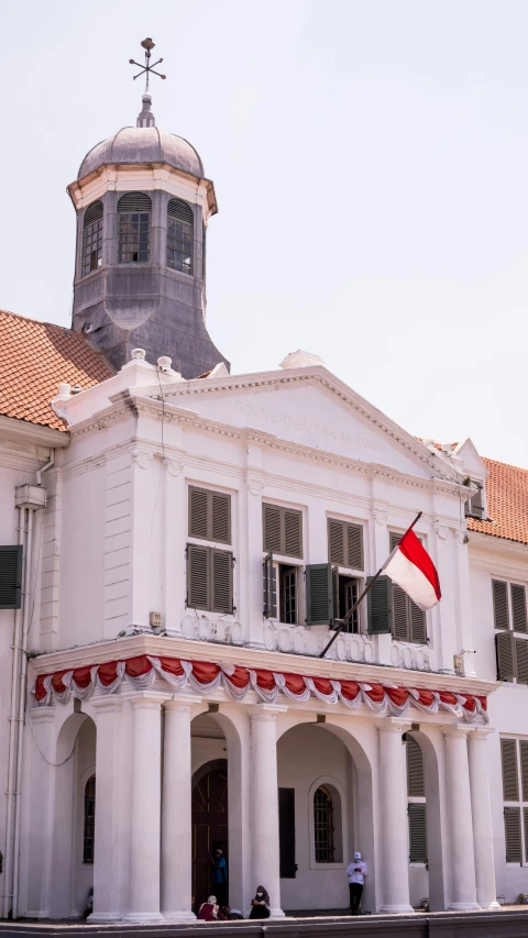 a large white building with a clock tower, inspired by Erik Pevernagie, trending on unsplash, red pennants, south jakarta, in balcony of palace, restoration