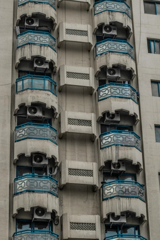 a tall building with blue balconies on the side of it, a photo, inspired by Ricardo Bofill, art nouveau, air conditioner, kowloon, slight overcast weather, medium-shot