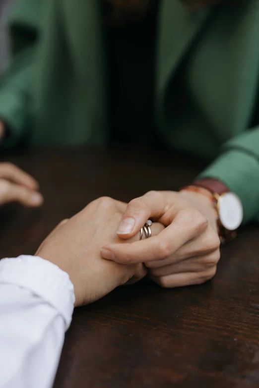 a man and a woman holding hands at a table, trending on unsplash, wearing green suit, hook as ring, lesbian, ignant