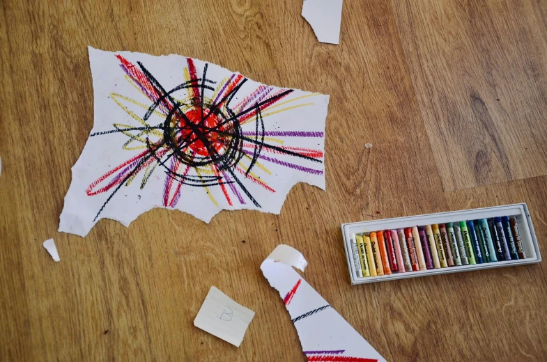 a piece of paper sitting on top of a wooden floor, inspired by Alexander Calder, pexels contest winner, crayon art, cracked, explosion drawing, tattered fabric, children drawing with pencils