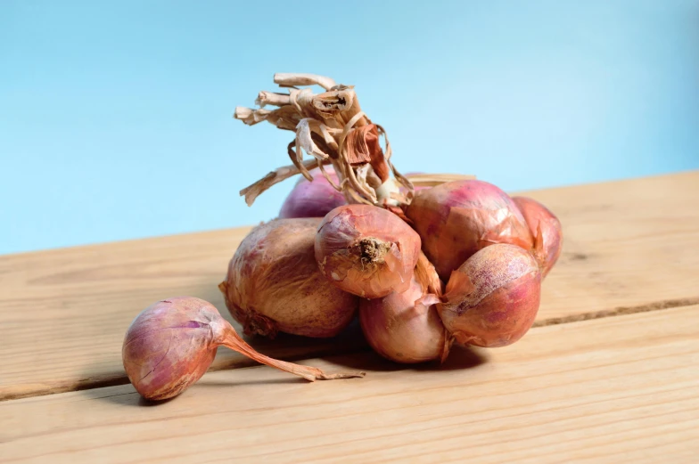 a pile of onions sitting on top of a wooden table, product photograph, blue, bashful expression, maroon