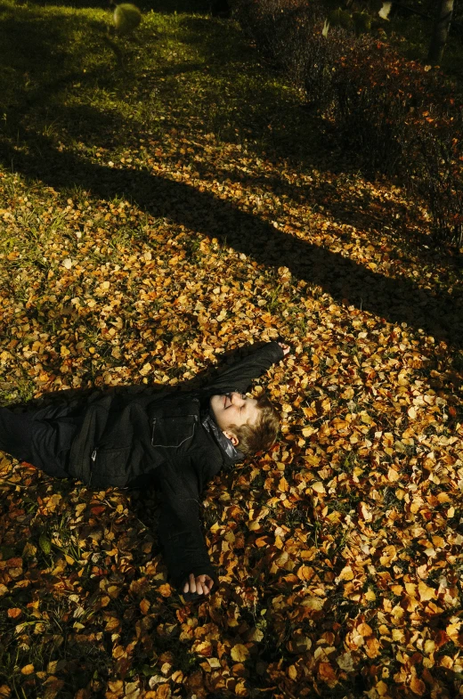 a person laying on the ground covered in leaves, striking a pose, taken in the late 2000s, autumn light, national geography photography