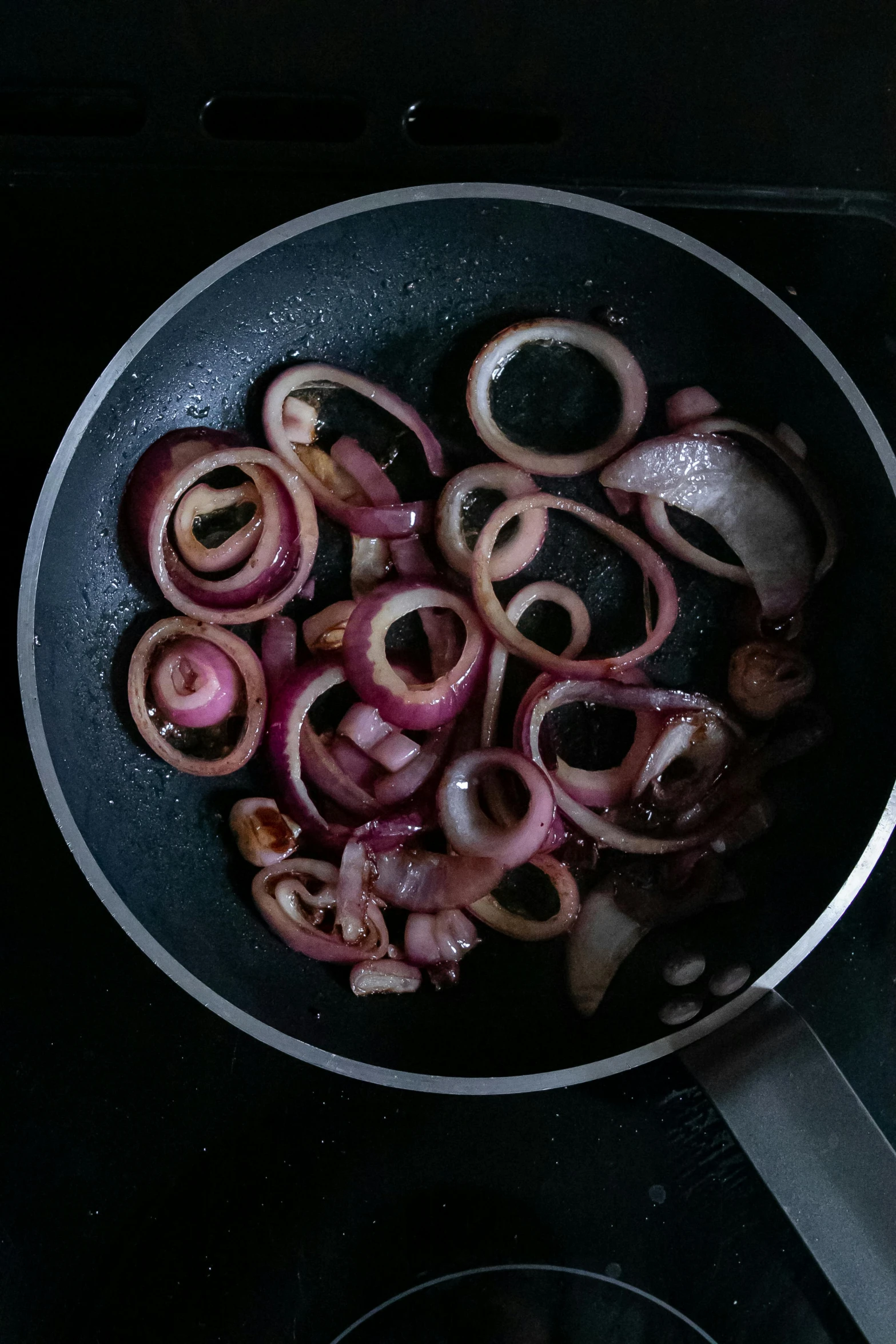 a frying pan filled with onions on top of a stove, by Alejandro Obregón, on a gray background, salad, convoluted, dark