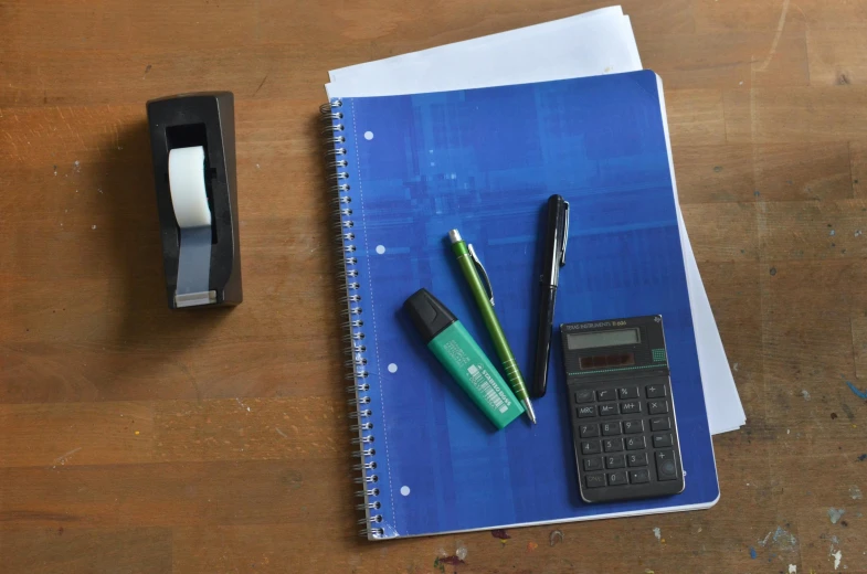 a blue notebook sitting on top of a wooden table next to a calculator, inspired by Gerard David, figuration libre, permanent marker, thumbnail, middle shot, educational supplies