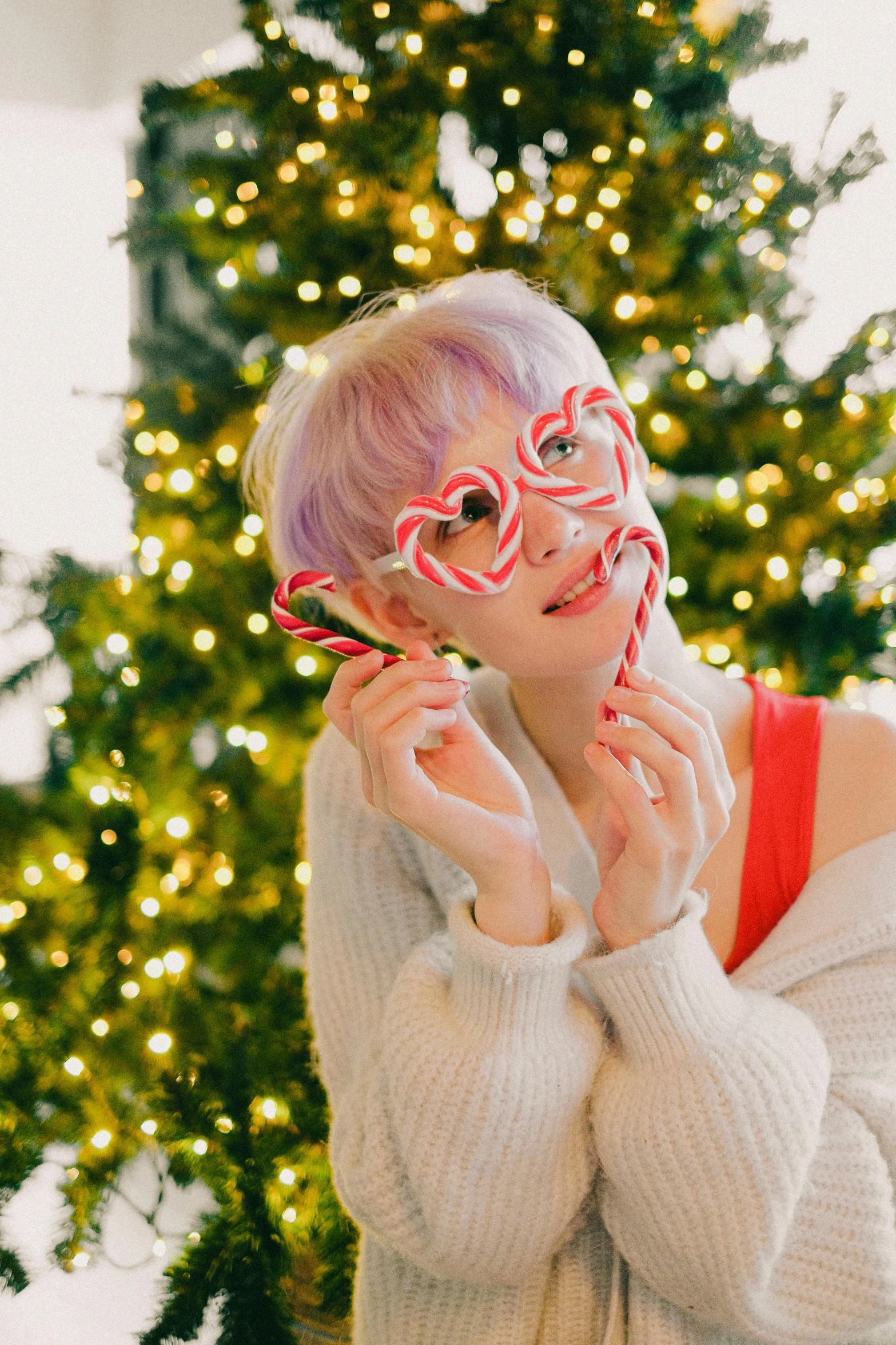 a woman holding a candy cane in front of a christmas tree, an album cover, by Kanbun Master, pexels, male ulzzang, pink glasses, heart eyes, jelly