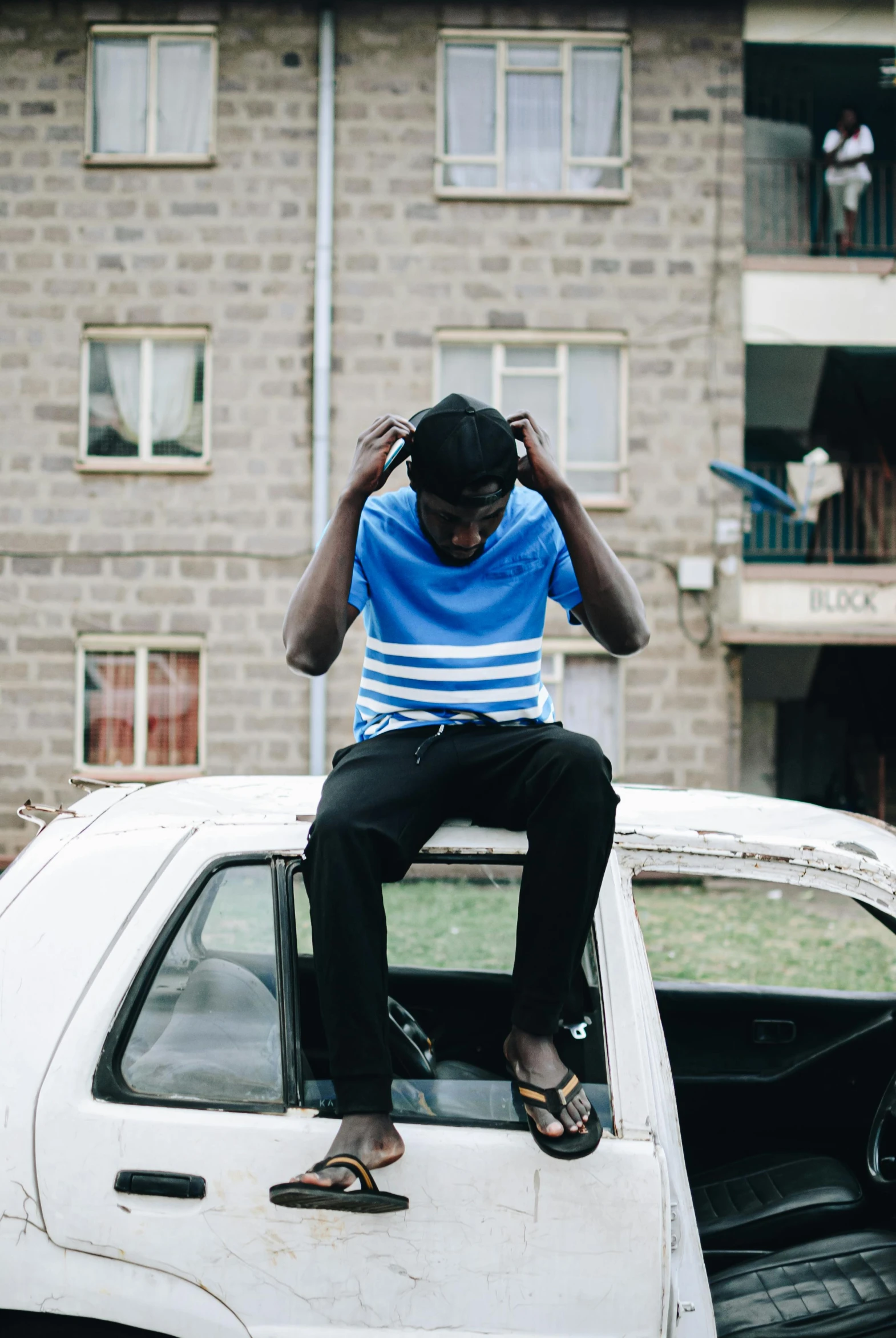 a man sitting on top of a white car, by Afewerk Tekle, trending on unsplash, happening, wearing ragged clothing, very kenyan, male teenager, concerned