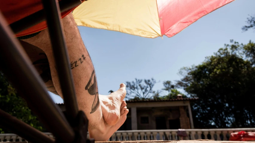 a man with a tattoo on his arm sitting under an umbrella, sol retreat, in the sun, profile image, são paulo