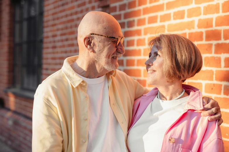 a man and a woman standing in front of a brick wall, by Lee Loughridge, pexels contest winner, older male, warm glow, looking upward, afternoon time