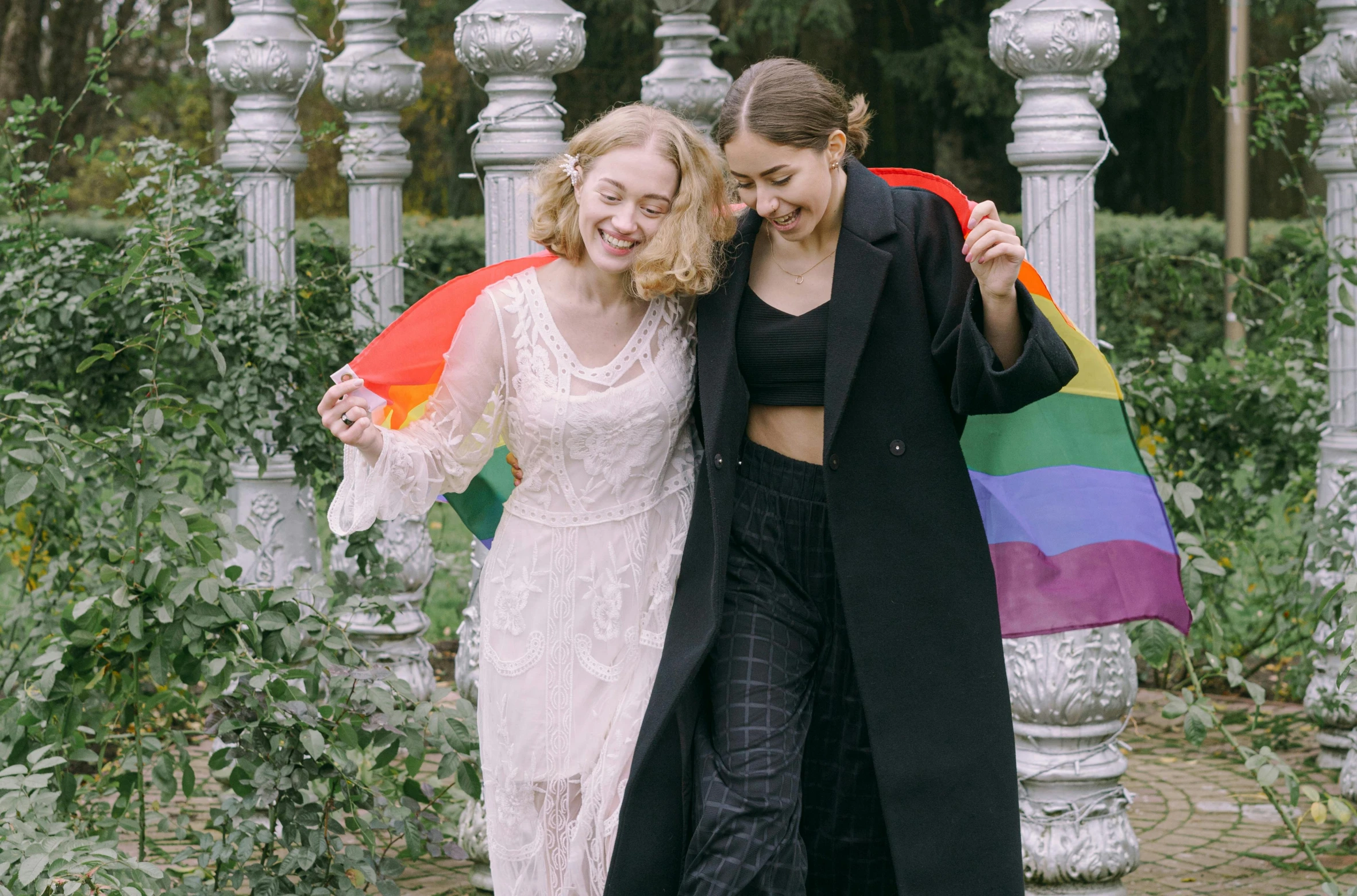 a couple of women standing next to each other, trending on pexels, renaissance, lgbt flag, delightful surroundings, wearing a long coat, celebration