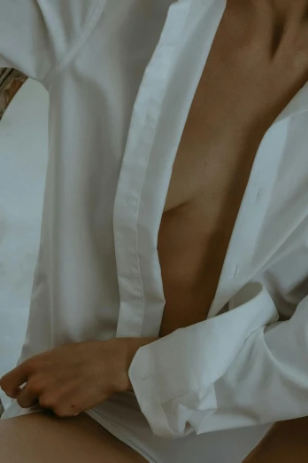 a woman in a white shirt sitting on a bed, an album cover, inspired by Elsa Bleda, trending on unsplash, decolletage, detail shot, open shirt, dress shirt