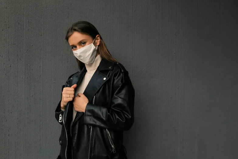 a woman wearing a face mask and leather jacket, a picture, trending on pexels, on a gray background, on a black wall, trenchcoat, healthcare