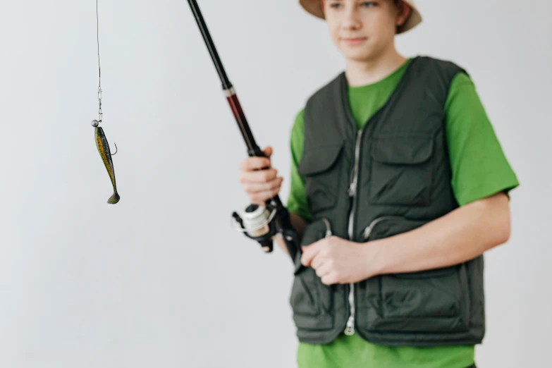 a boy in a green shirt is holding a fishing rod, trending on pexels, hurufiyya, wearing a vest, 1 6 years old, lachlan bailey, concept photo