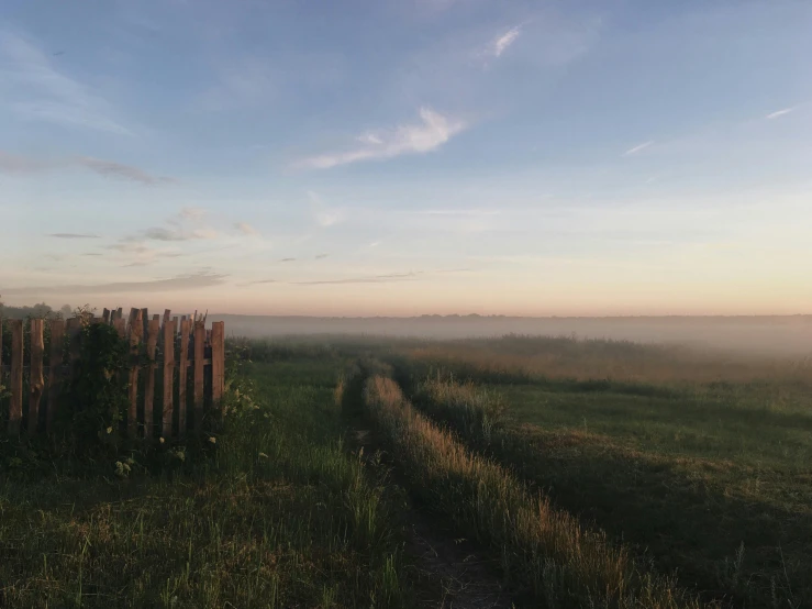 a wooden fence sitting in the middle of a field, by Attila Meszlenyi, pexels contest winner, eden at dawn, humid evening, clear skies in the distance, slight fog