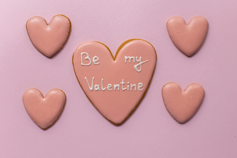 a heart shaped cookie with the words be my valentine written on it, trending on pexels, background image, mauve background, aleksandra waliszewska, feature