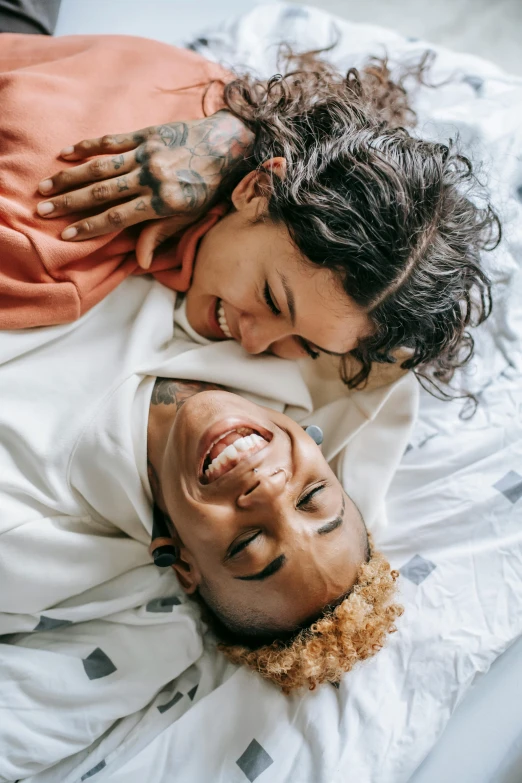 a man and a woman laying on top of a bed, by Cosmo Alexander, trending on pexels, lesbian embrace, smiling laughing, ashteroth, tattooed