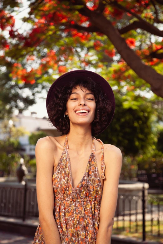 a woman in a dress and hat sitting on a bench, trending on pexels, dark short curly hair smiling, orange halter top, hippy, ad image