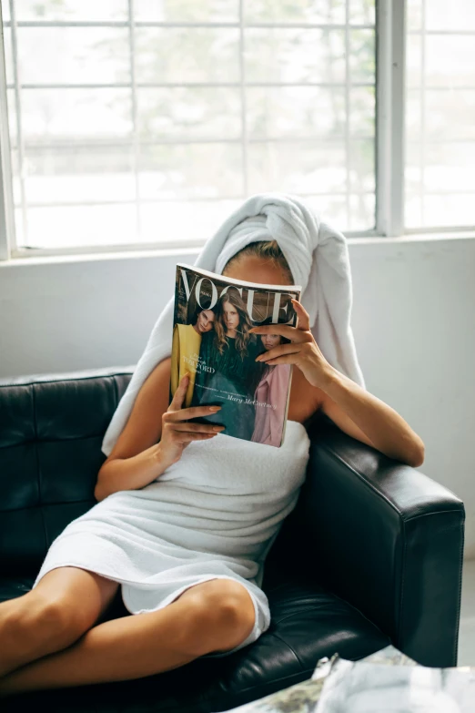 a woman sitting in a chair reading a magazine, by Robbie Trevino, pexels contest winner, happening, wearing a towel, over it's head, vogue cover, gif