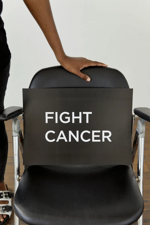 a woman standing next to a chair with a sign on it, by Dan Frazier, pexels contest winner, the cure for cancer, close-up fight, black main color, getting ready to fight