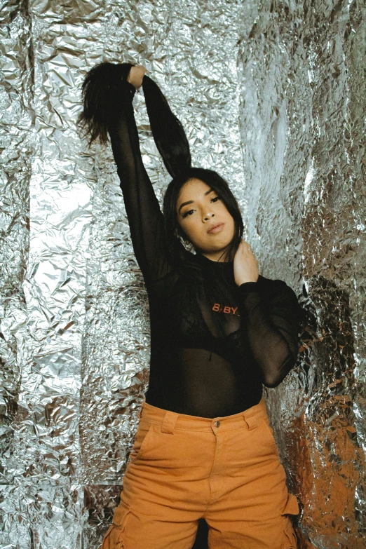 a woman in a black top and orange pants, an album cover, inspired by Elsa Bleda, trending on pexels, shiny silver, shooting pose, see through, gongbi