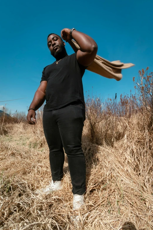 a man standing in a field holding a bag, an album cover, pexels contest winner, man is with black skin, wearing jeans and a black hoodie, 15081959 21121991 01012000 4k, dynamic low angle shot