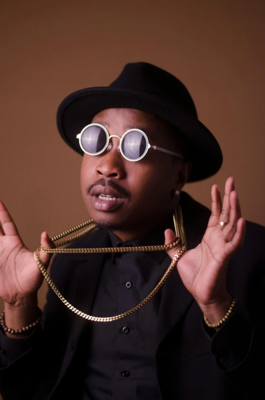 a close up of a person wearing a hat and glasses, an album cover, inspired by Zhu Da, trending on pexels, neo-dada, sam hyde in gold suit, sassy pose, wearing gold chain, rubenesque