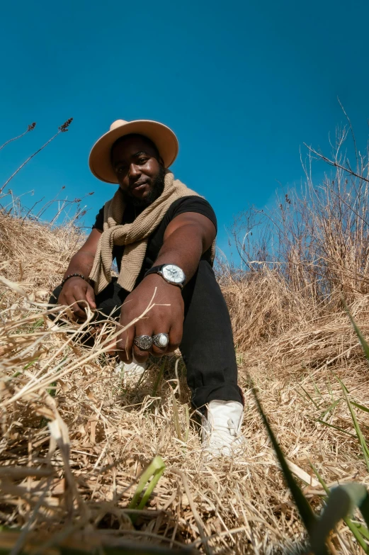 a man sitting on top of a pile of dry grass, an album cover, by Nyuju Stumpy Brown, standing in tall grass, press photos, at an archaeological dig site, kezie demessance