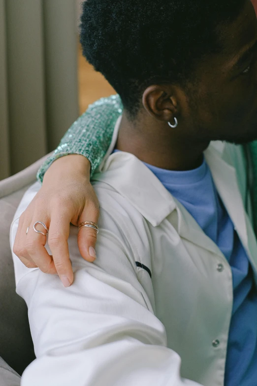 a man sitting next to a woman on a couch, by Winona Nelson, trending on pexels, romanticism, wearing two metallic rings, with a lab coat, arm around her neck, teal aesthetic