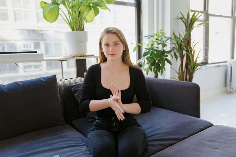 a woman sitting on a couch in a living room, a portrait, by Nina Hamnett, unsplash, partially cupping her hands, sydney sweeney, serpentine pose gesture, sitting on a lab table