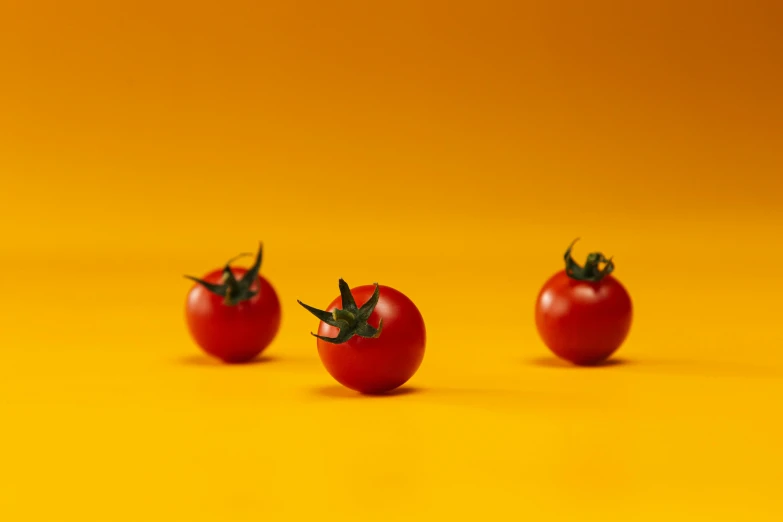 three tomatoes sitting on top of a yellow surface, pexels contest winner, taken with sony alpha 9, metaballs, trending on dezeen, cinematic full shot